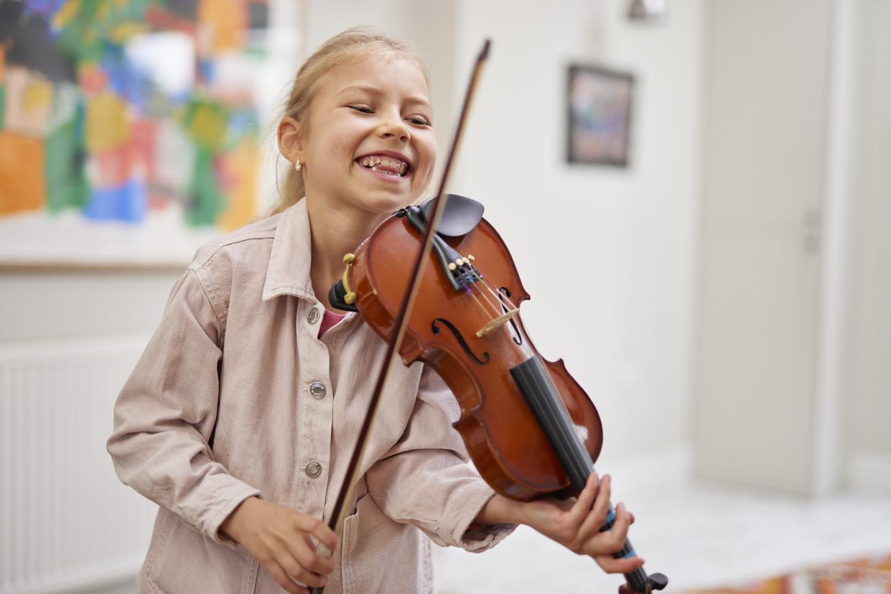 Happy young student holding violin and bow